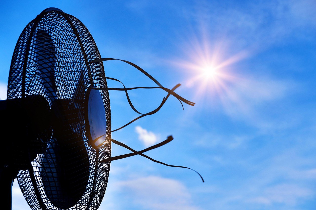 Pales d'un ventilateur à contre-jour sous un soleil éclatant, symbole de la lutte contre la chaleur